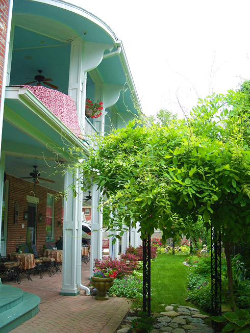 View of the veranda, porch and side yard, showing tables, chairs and whisteria arch